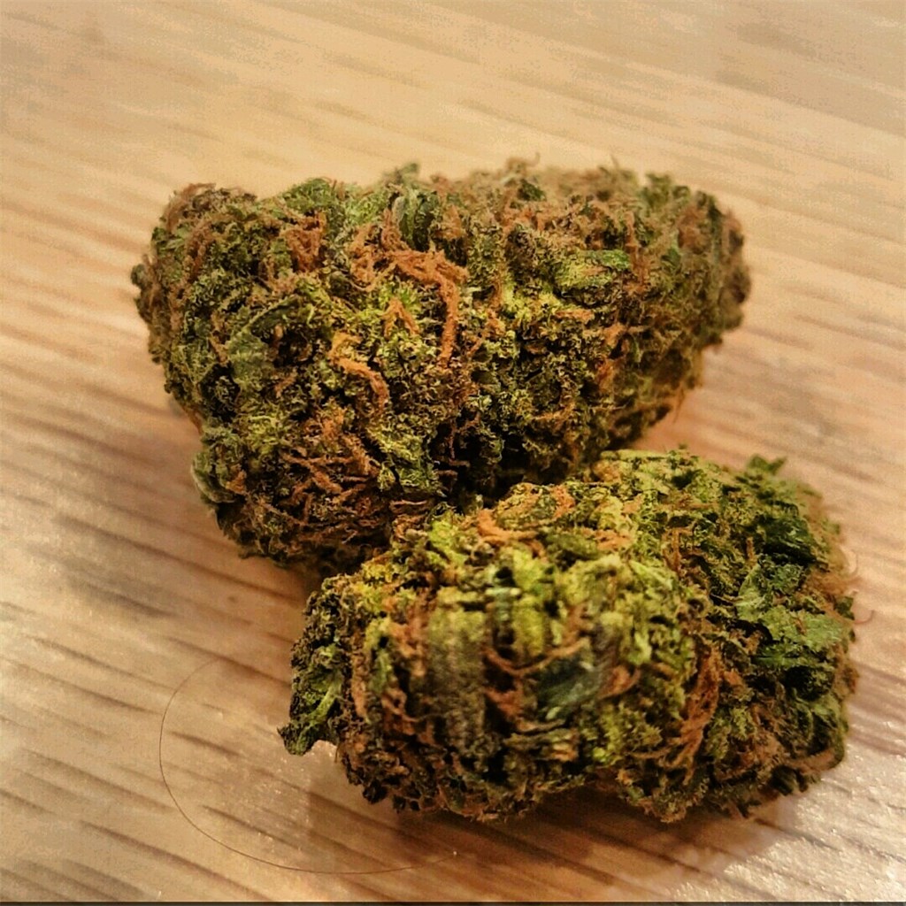 Two smaller, dense nugs of the Durban Poison cannabis strain sit together on a wood table. Via Leafly.com